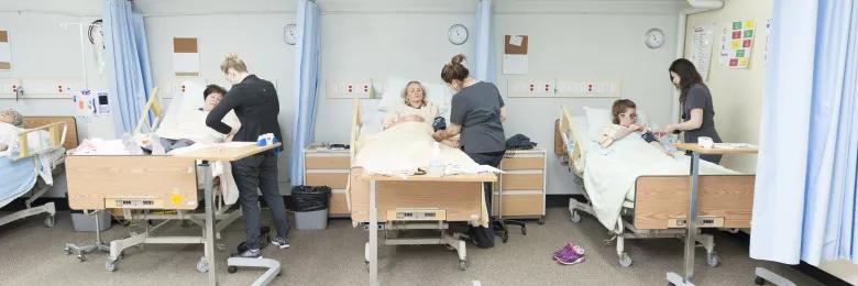 Nursing students in lab assisting patients at hospital beds